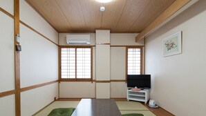 A traditional Japanese room with tatami flooring, a low table, and a television on a white stand. - Tabist Beppu kitahama no yado ao (Beppu)