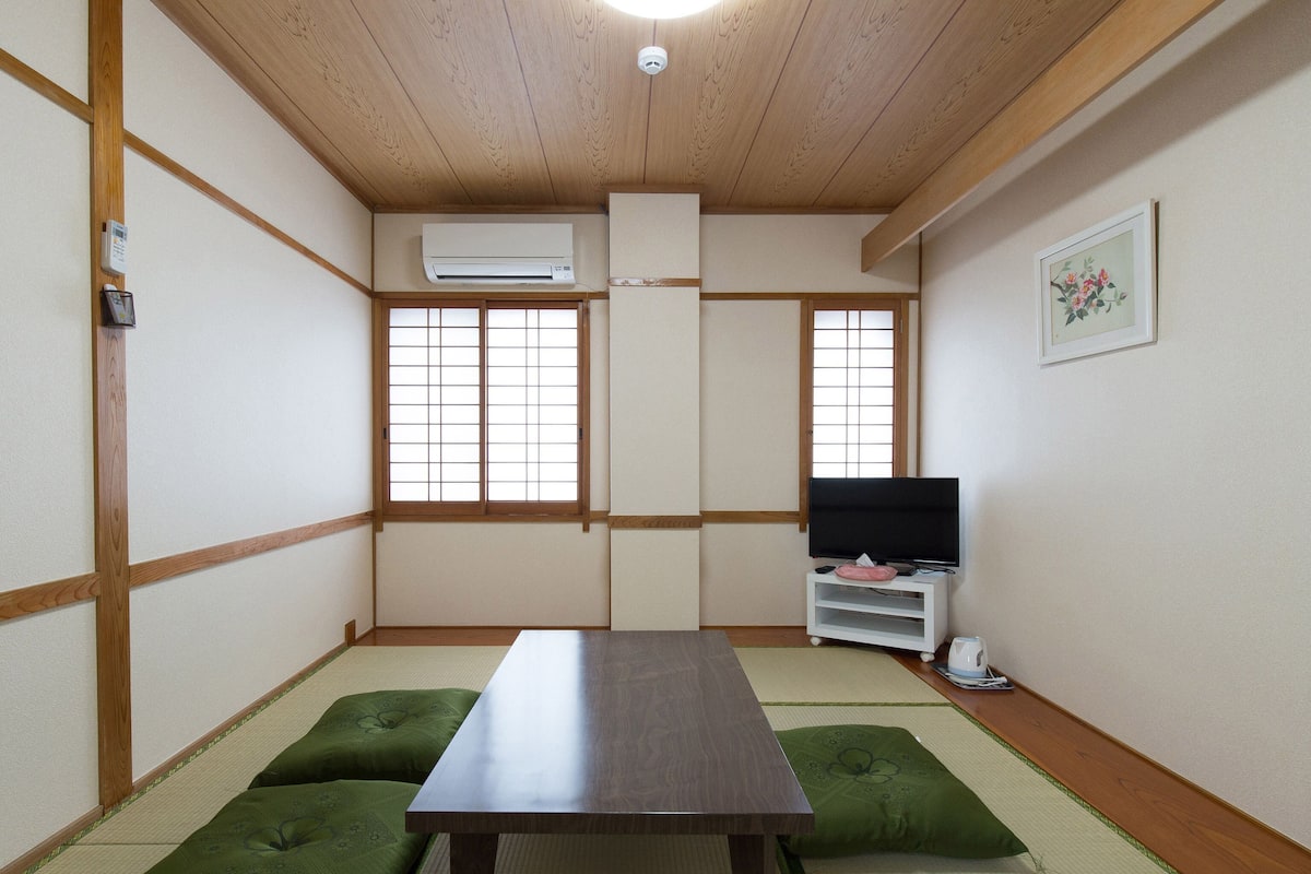 Une pièce de style japonais traditionnel, avec un sol recouvert de tatamis, une table basse et un téléviseur posé sur un meuble blanc.