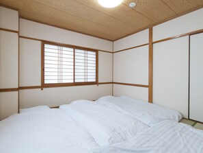 Quarto com teto de madeira, janela com molduras de madeira e cama com roupa de cama branca.