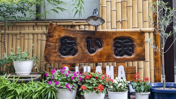 A wooden sign with Japanese characters, surrounded by potted plants and a bamboo fence. - Tabist Beppu kitahama no yado ao (Beppu)