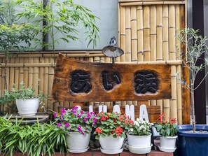 A wooden sign with Japanese characters, surrounded by potted plants and a bamboo fence. - Tabist Beppu kitahama no yado ao (Beppu)