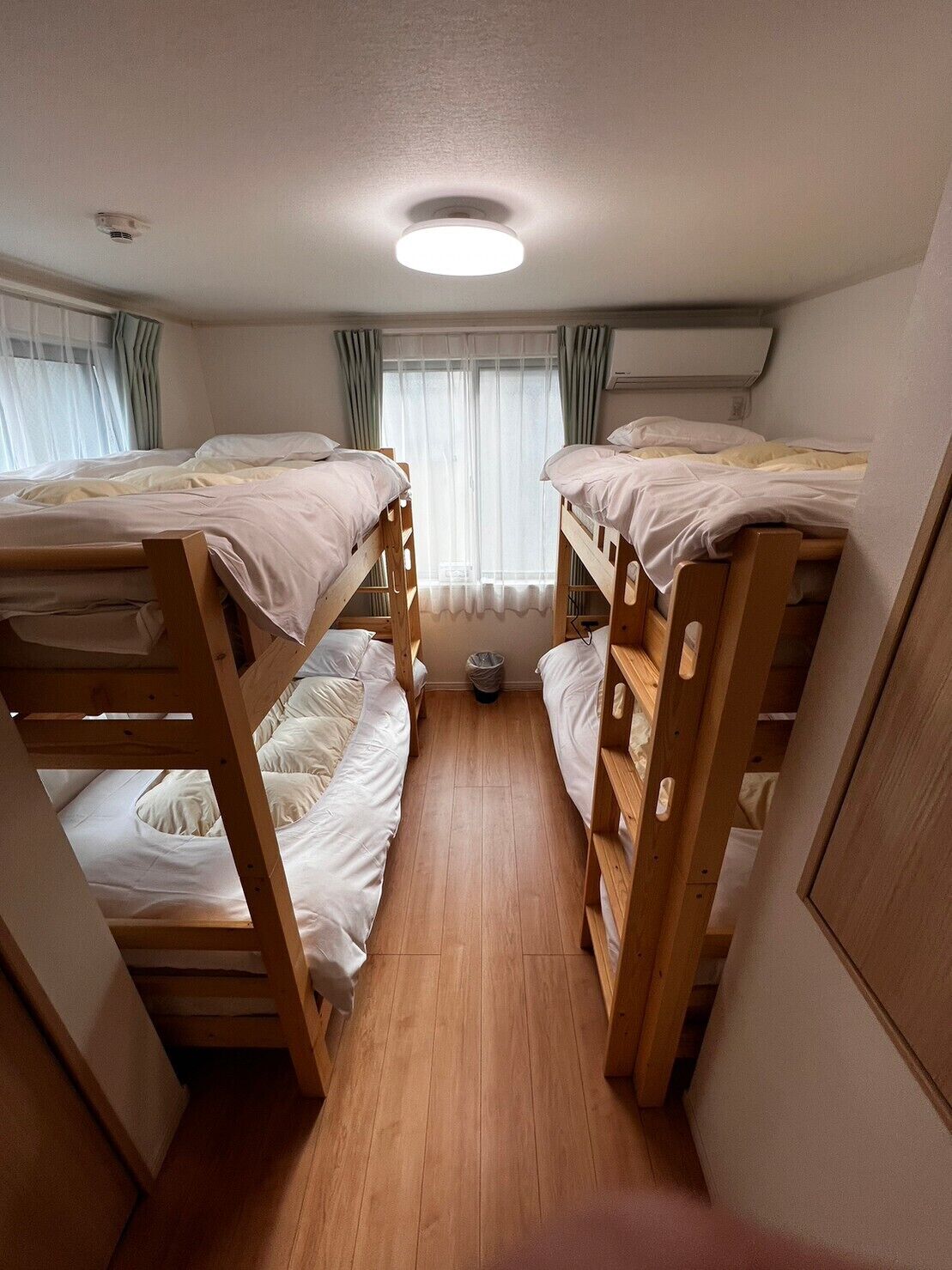 A compact room with two bunk beds, a small window with curtains, a radiator, and a ceiling light.