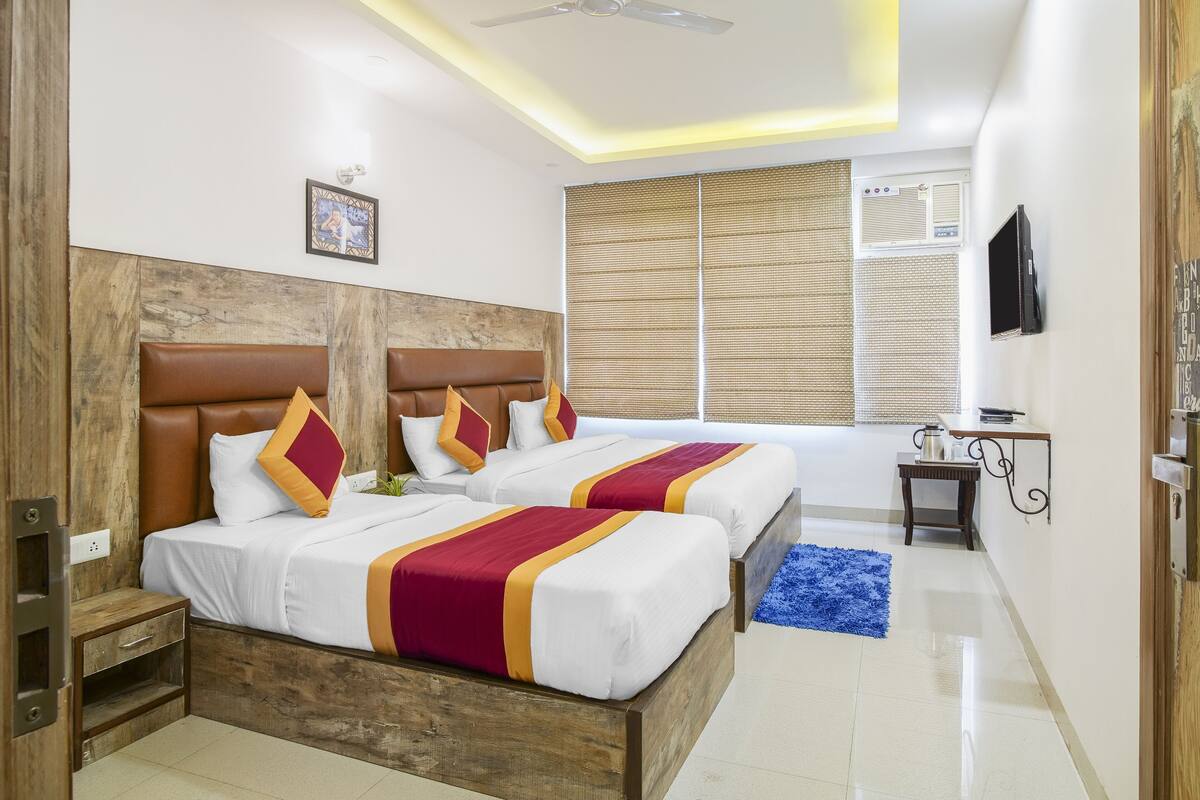 Une chambre d’hôtel avec deux lits, des têtes de lit en bois, une petite table de chevet, un tapis bleu et un téléviseur fixé au mur.