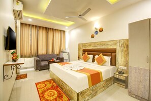 A hotel room with a bed, a sofa, a desk, an air conditioner, a ceiling fan, and a television. - Gracious by Vishesh Hotels & Home Stay (New Delhi)