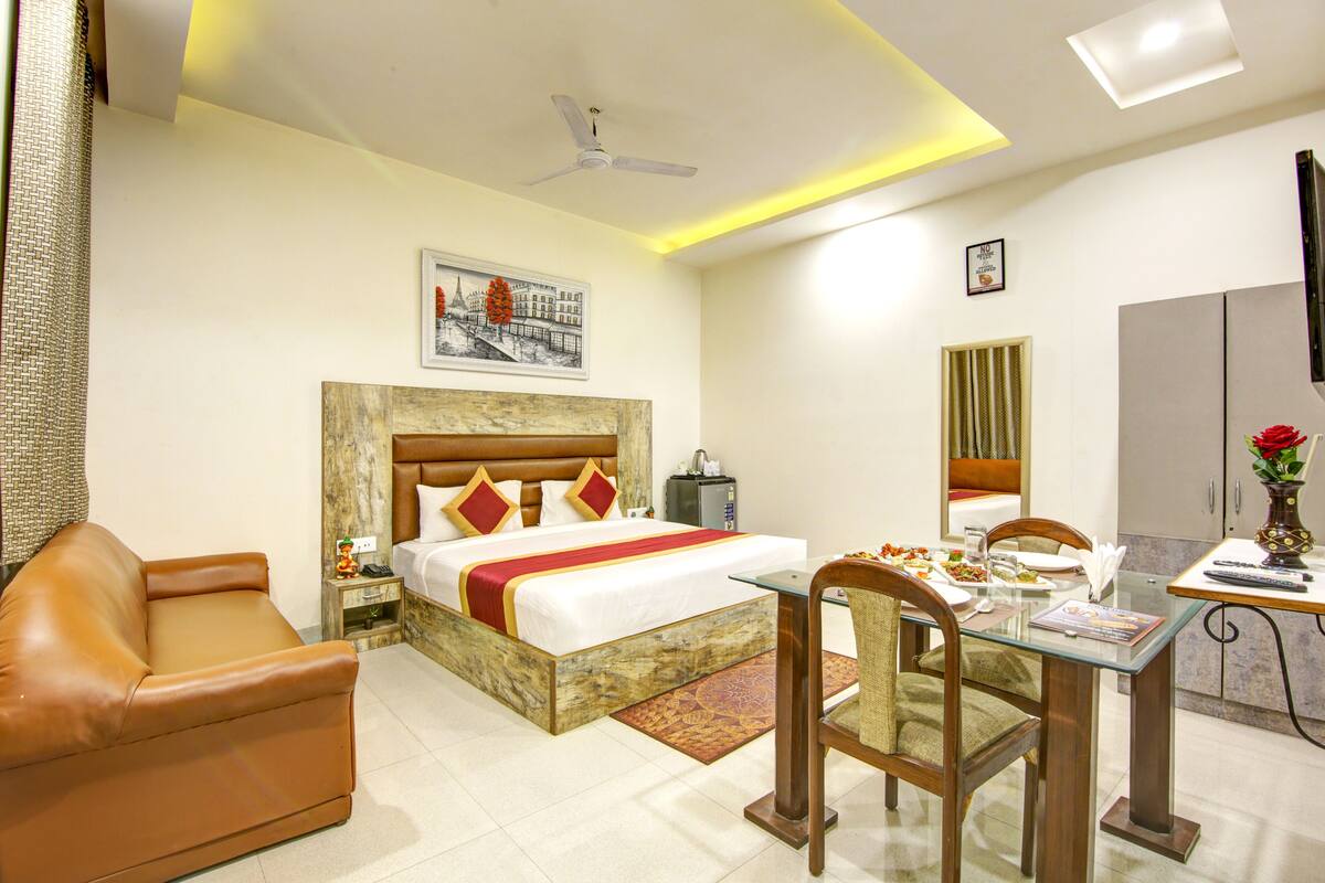 Une chambre d’hôtel comprenant un lit, un canapé en cuir, une table à manger avec des chaises, un téléviseur et un ventilateur de plafond.
