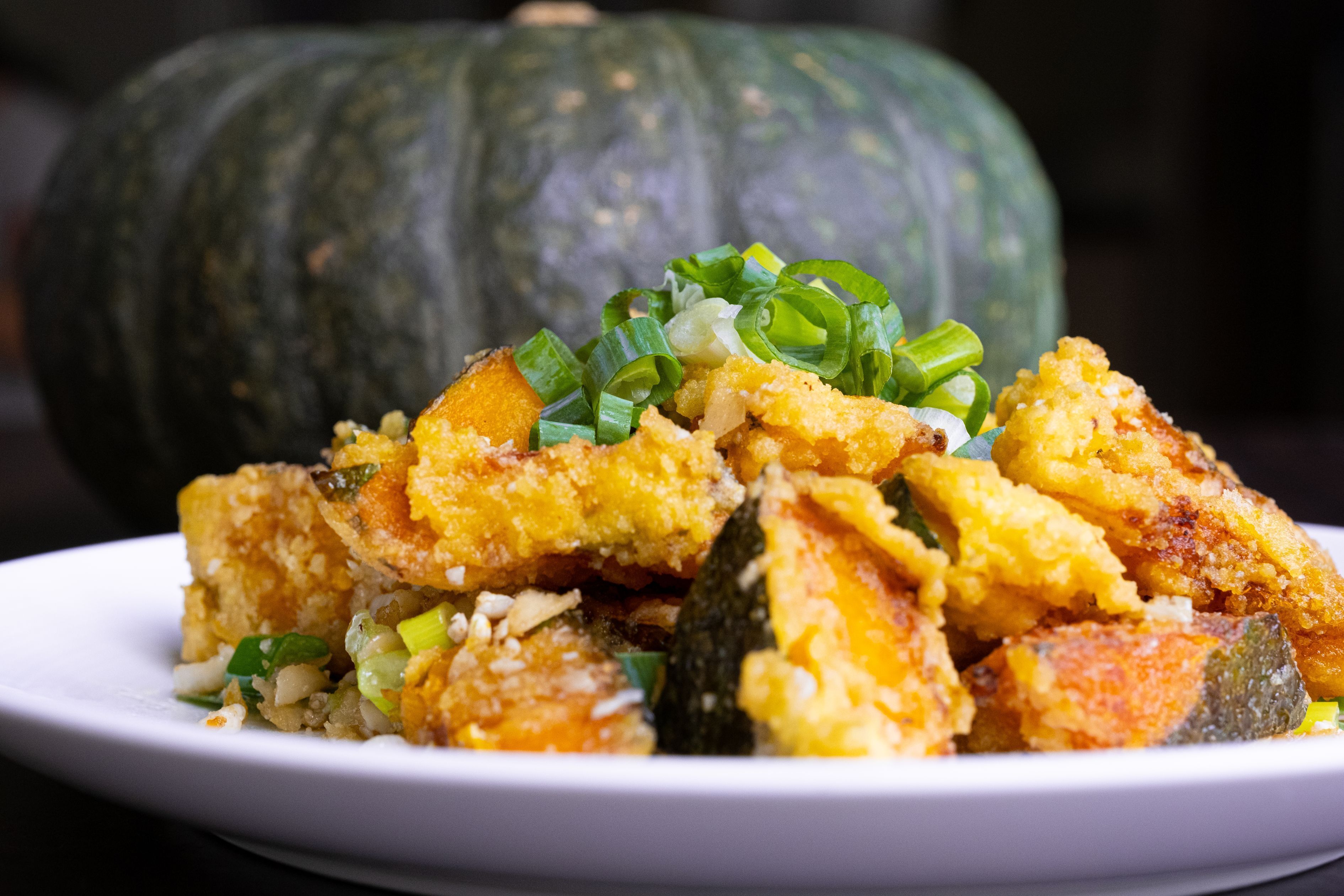 Un plato de comida frita con cebollines, frente a una calabaza.