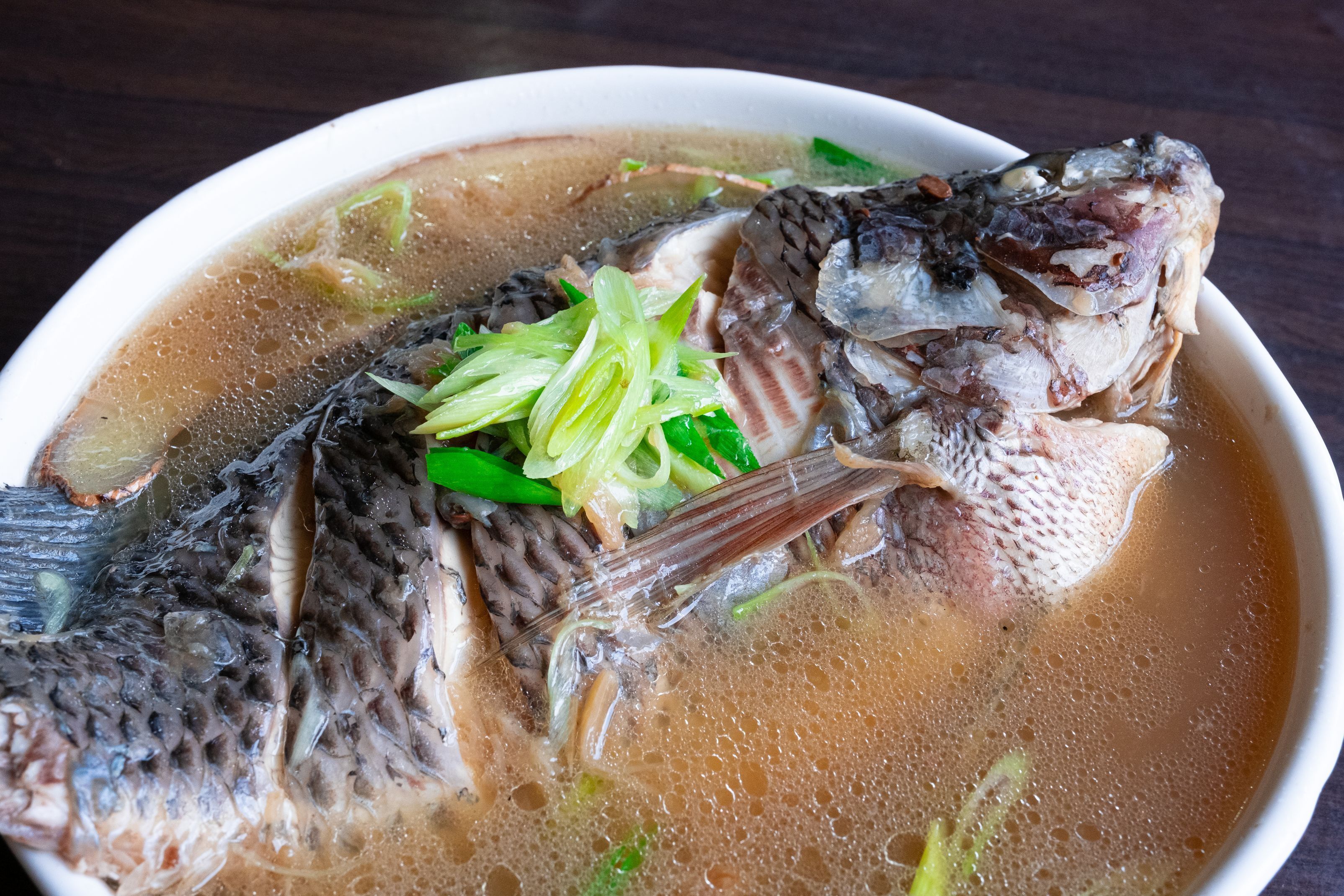 En skål fiskesuppe med synlige fiskeben og grønne forårsløg.