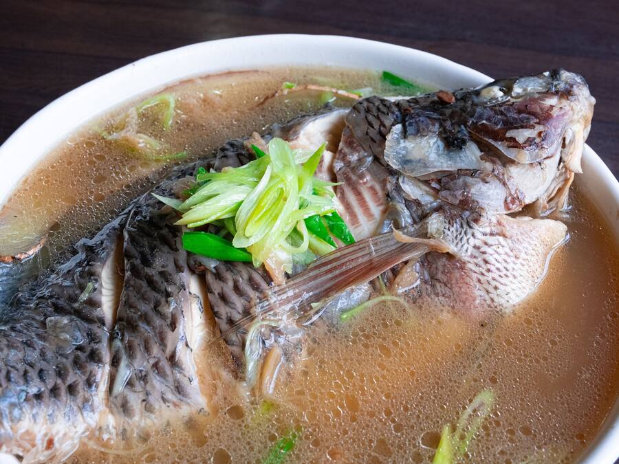 En skål fiskesuppe med synlige fiskeben og grønne forårsløg.