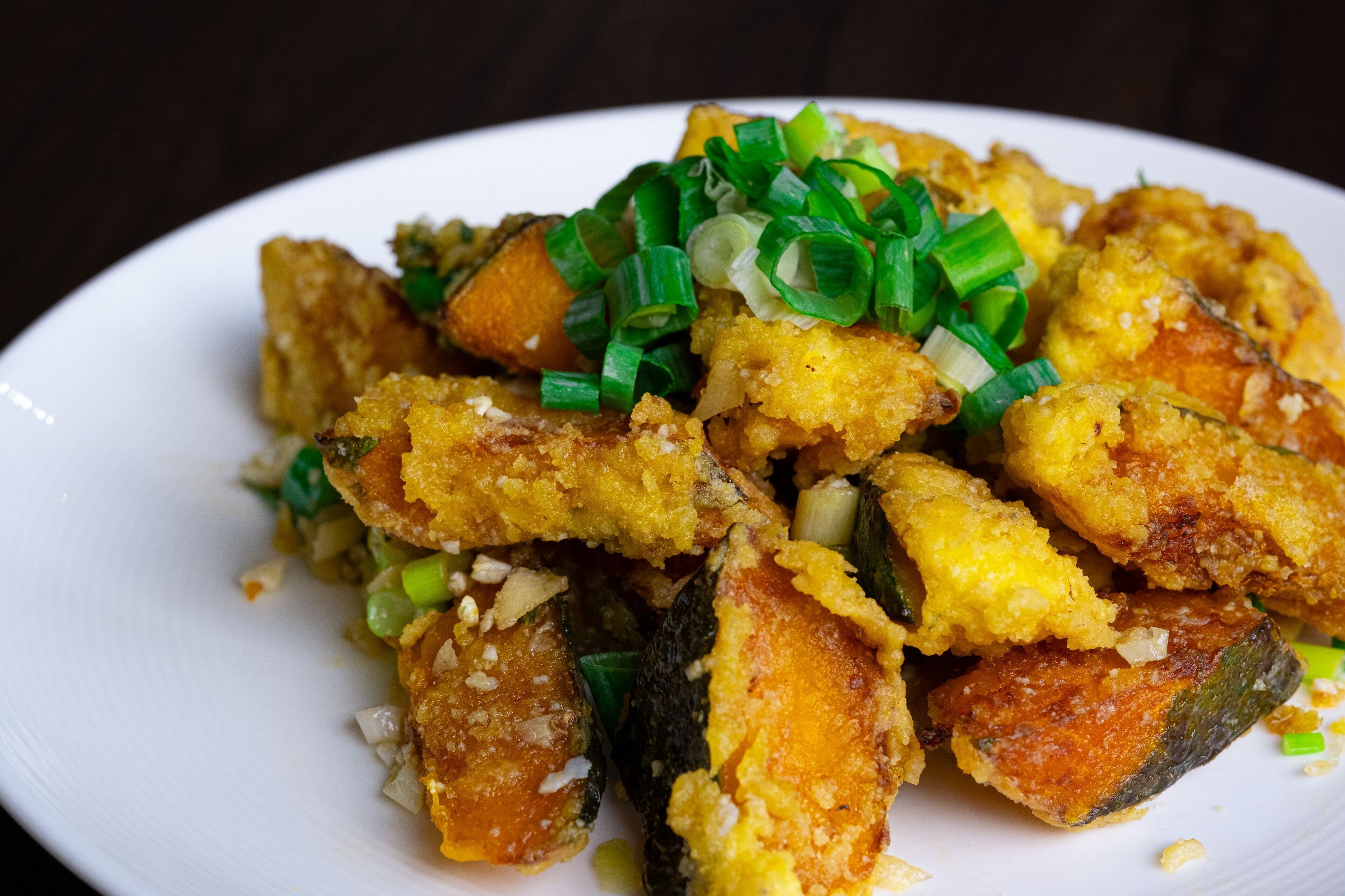 A plate of fried food with green onions on top.