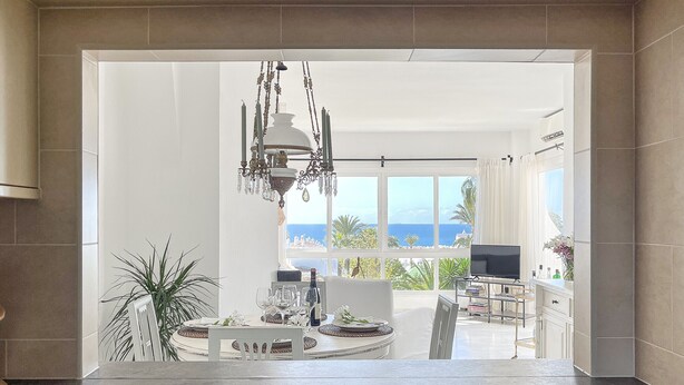 A modern kitchen with a dining area, large windows with a view of the ocean, and a chandelier. - J07 Jardines 4 - Apartment with sea views (Sitio de Calahonda)