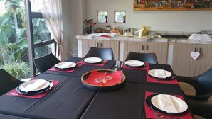 Un comedor con una mesa preparada para cuatro, una cocina al fondo y un mural en la pared.