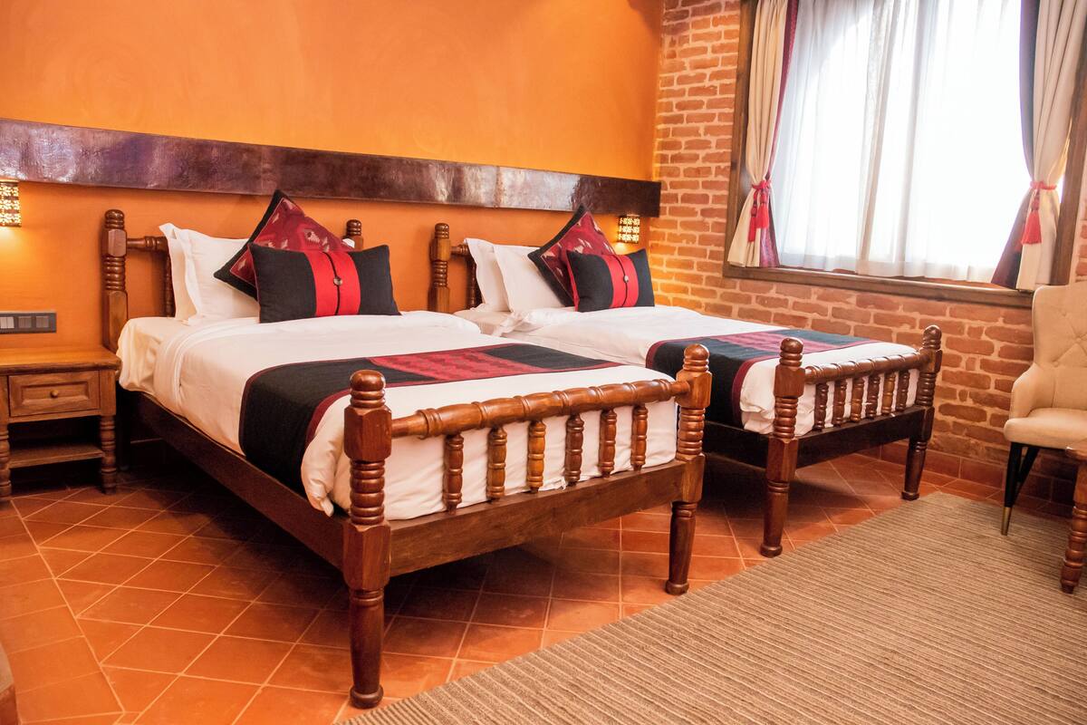 A double bed with a wooden frame and a headboard, a nightstand, and a chair in a room with orange walls and a brick accent wall.