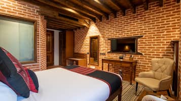 Un dormitorio con una cama grande, techo de madera, pared de ladrillo, televisor, una silla y un escritorio.