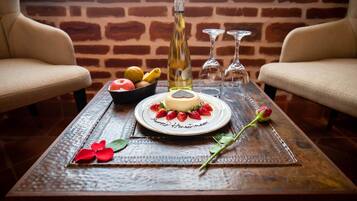 Un tavolo con un dessert, una bottiglia e dei bicchieri, sullo sfondo di un muro in mattoni con due poltrone.