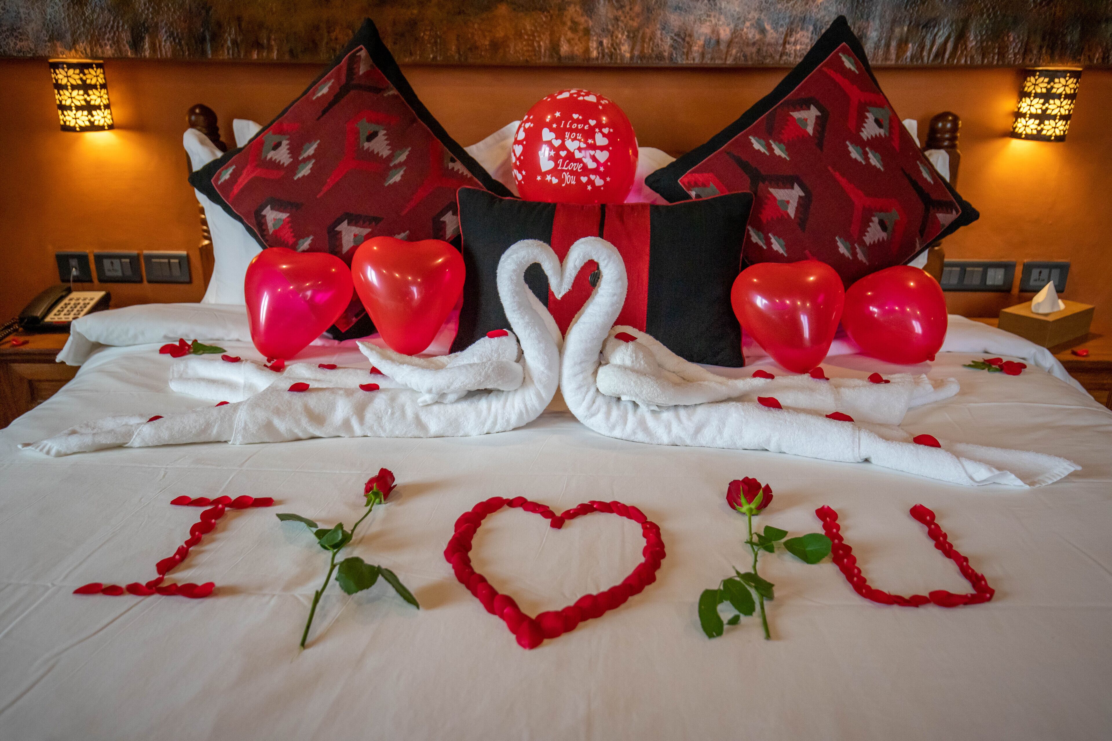 Cama com rosas vermelhas e decorações em formato de coração, incluindo um coração feito de rosas e um desenho de cisne com toalhas.