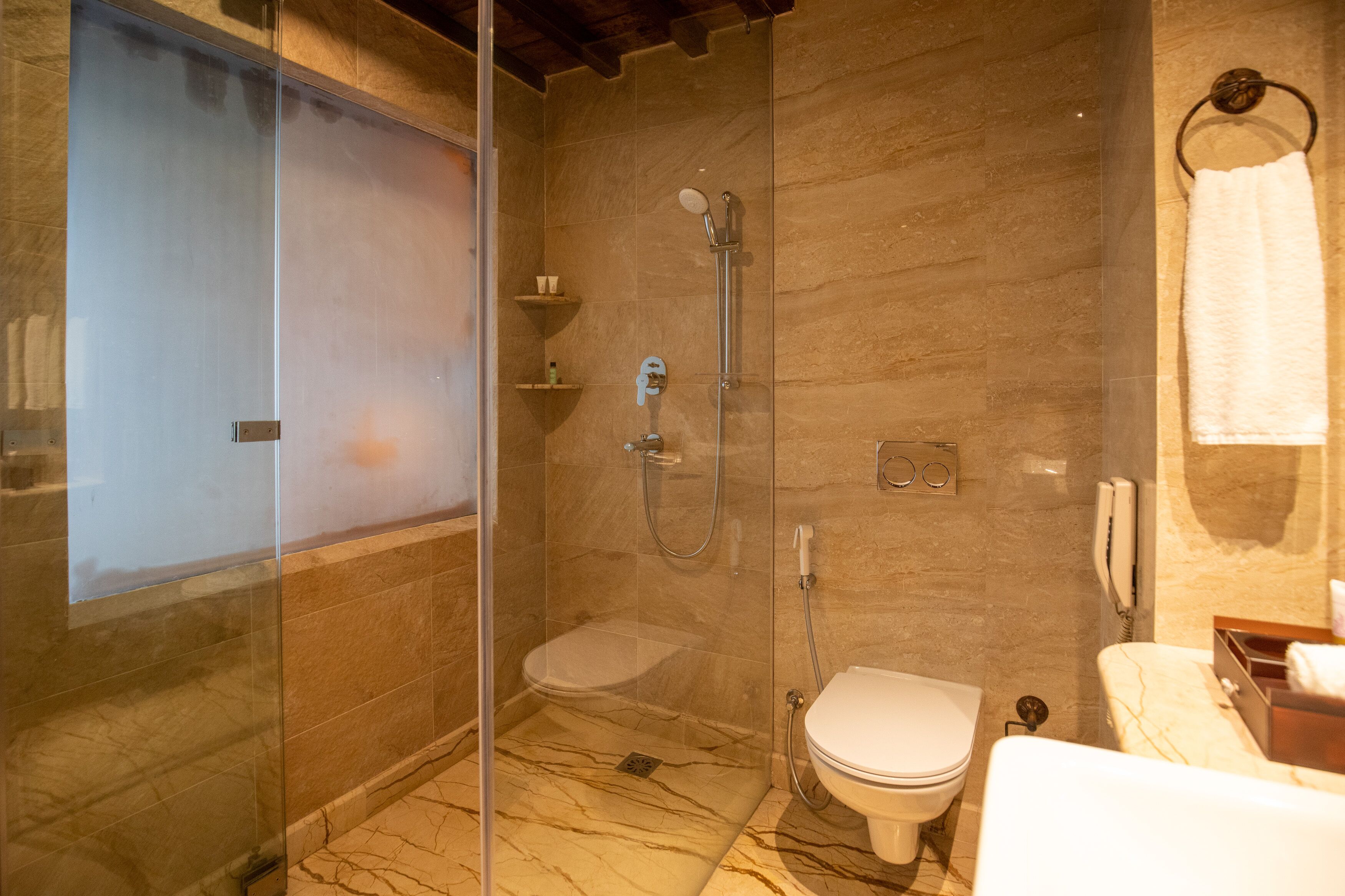 A modern bathroom with a glass-enclosed shower, a toilet, and a marble floor.