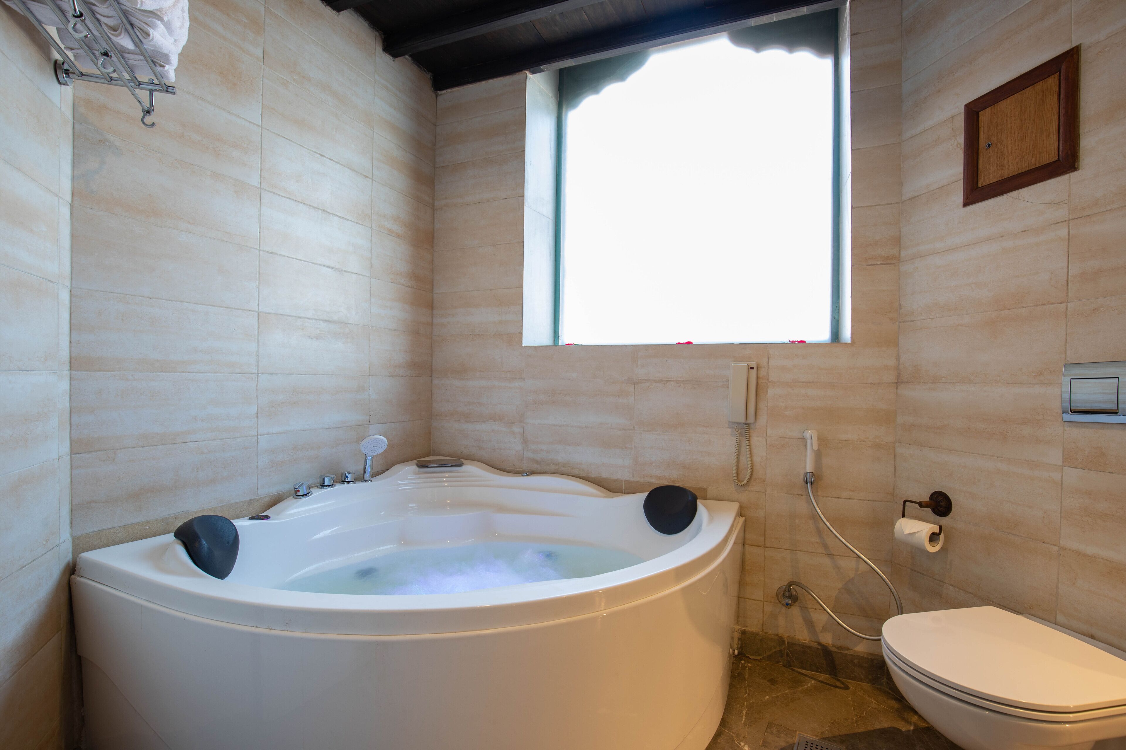 A bathroom with a large bathtub, a toilet, and a window providing natural light.