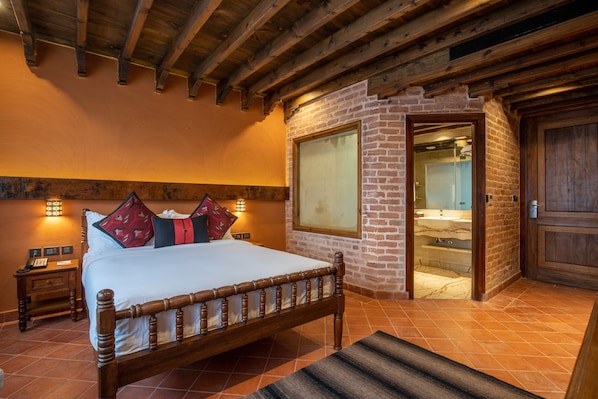 Una cama de madera con cabecera, una mesita de noche con un teléfono y un baño visible a través de una puerta abierta.