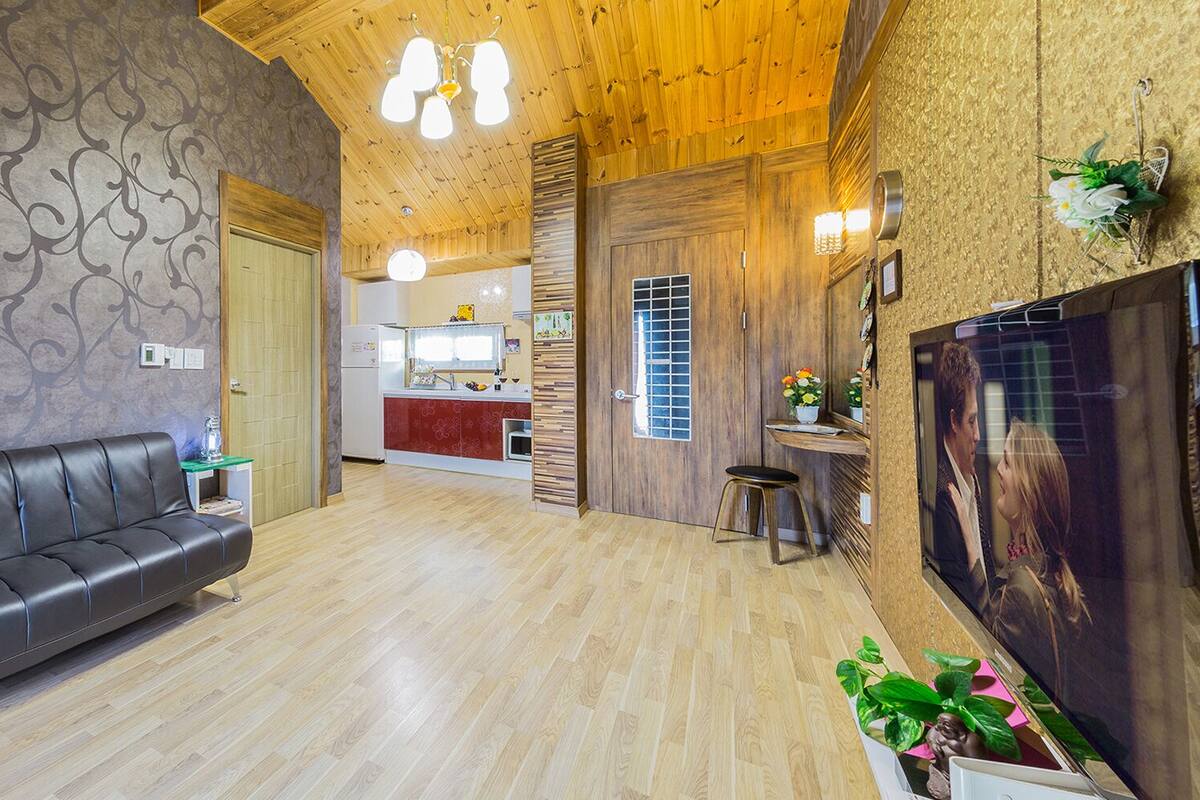A modern interior with a leather sofa, wooden flooring, a kitchen area, and a TV mounted on the wall.