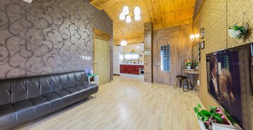 Un interior moderno con un sofá de cuero, suelo de madera, una zona de cocina y un televisor montado en la pared.