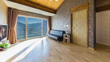 A spacious room with a large window, a sofa, a wooden door, and a television.