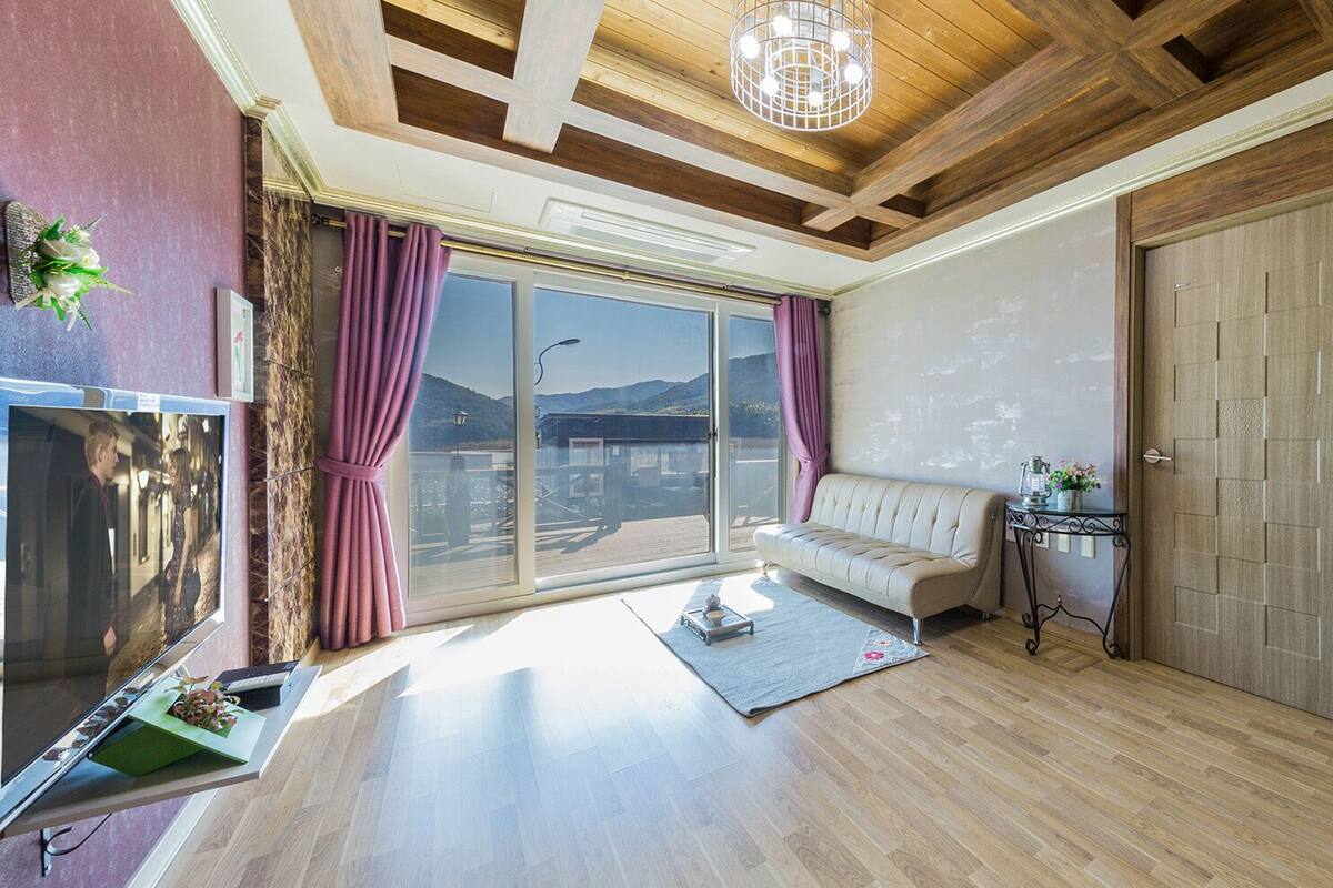 A spacious living room with a large window, a sofa, a small table, and a TV.