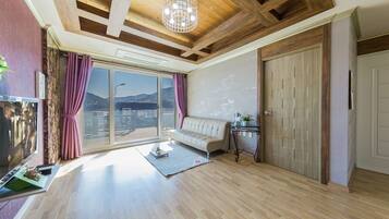 A spacious living room with a large window, a sofa, a small table, and a TV.