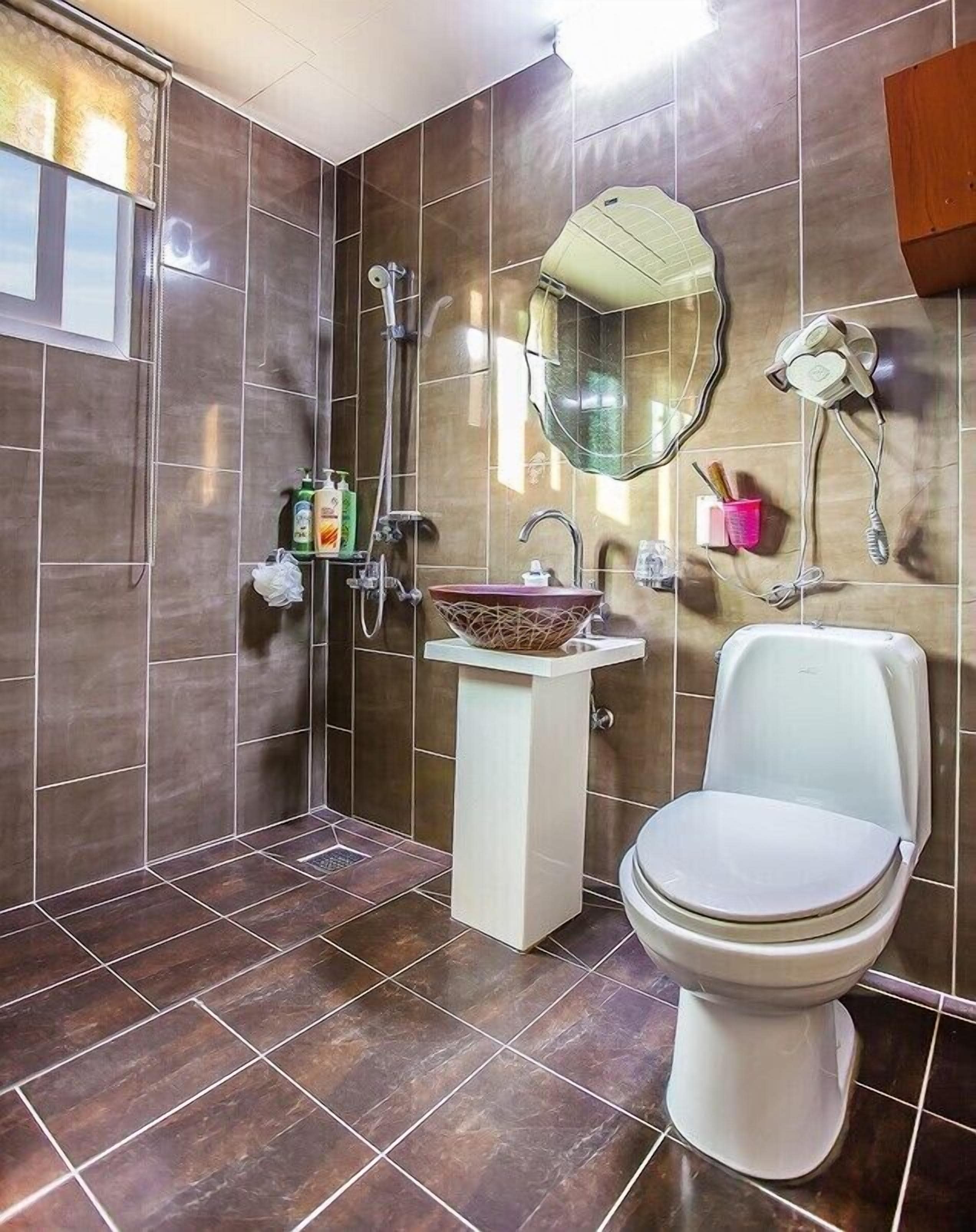 A bathroom with a modern design, featuring a large mirror, a vessel sink, a toilet, and a shower area.
