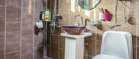 A bathroom with a modern design, featuring a large mirror, a vessel sink, a toilet, and a shower area.
