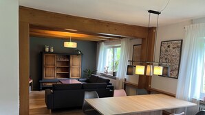 Un espace repas moderne avec une table et des chaises en bois, un canapé et un meuble sur lequel on peut lire le mot « AUERLAND ».