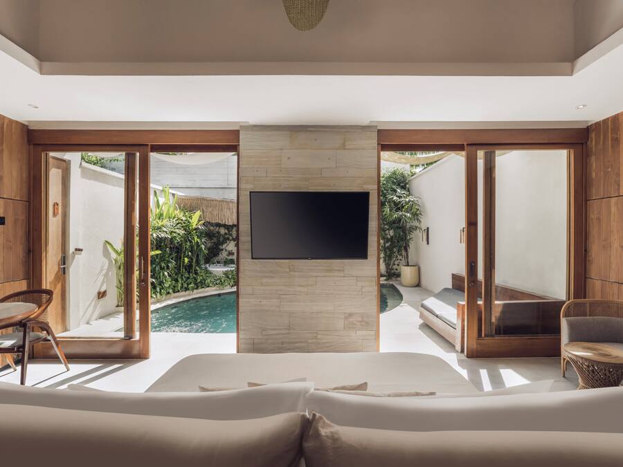 A modern room with a large bed, a TV mounted on a stone wall, and a pool visible through the glass doors.