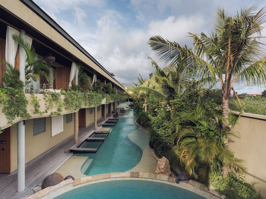 A pool area with a water channel, surrounded by lush greenery and palm trees.