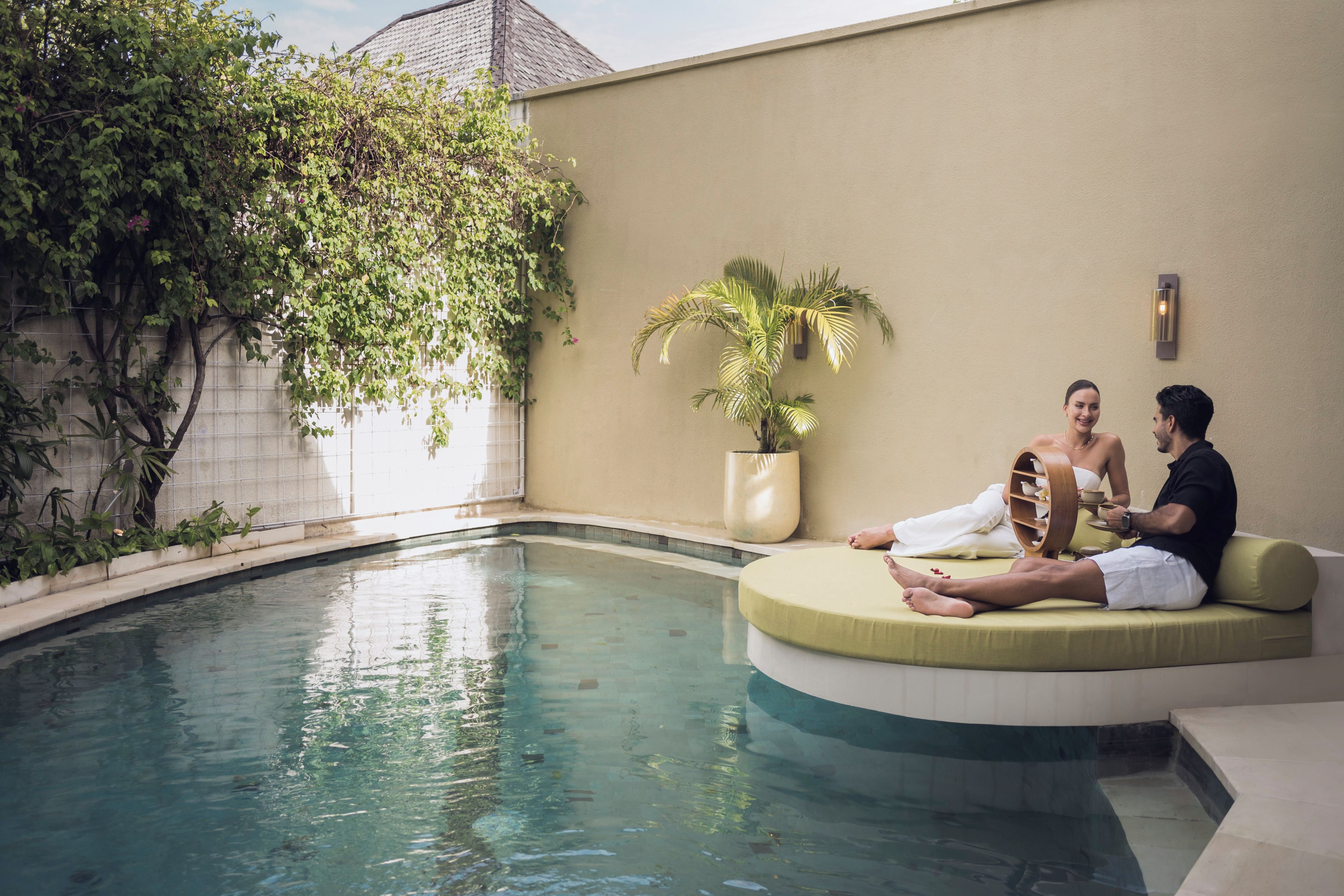 A poolside area with a curved seating area, a potted plant, and a wall-mounted light fixture.