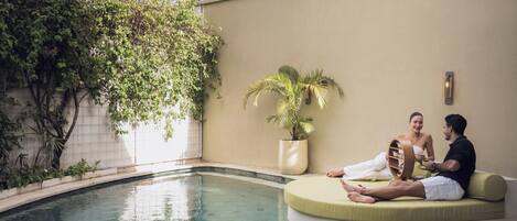 A poolside area with a curved seating area, a potted plant, and a wall-mounted light fixture.