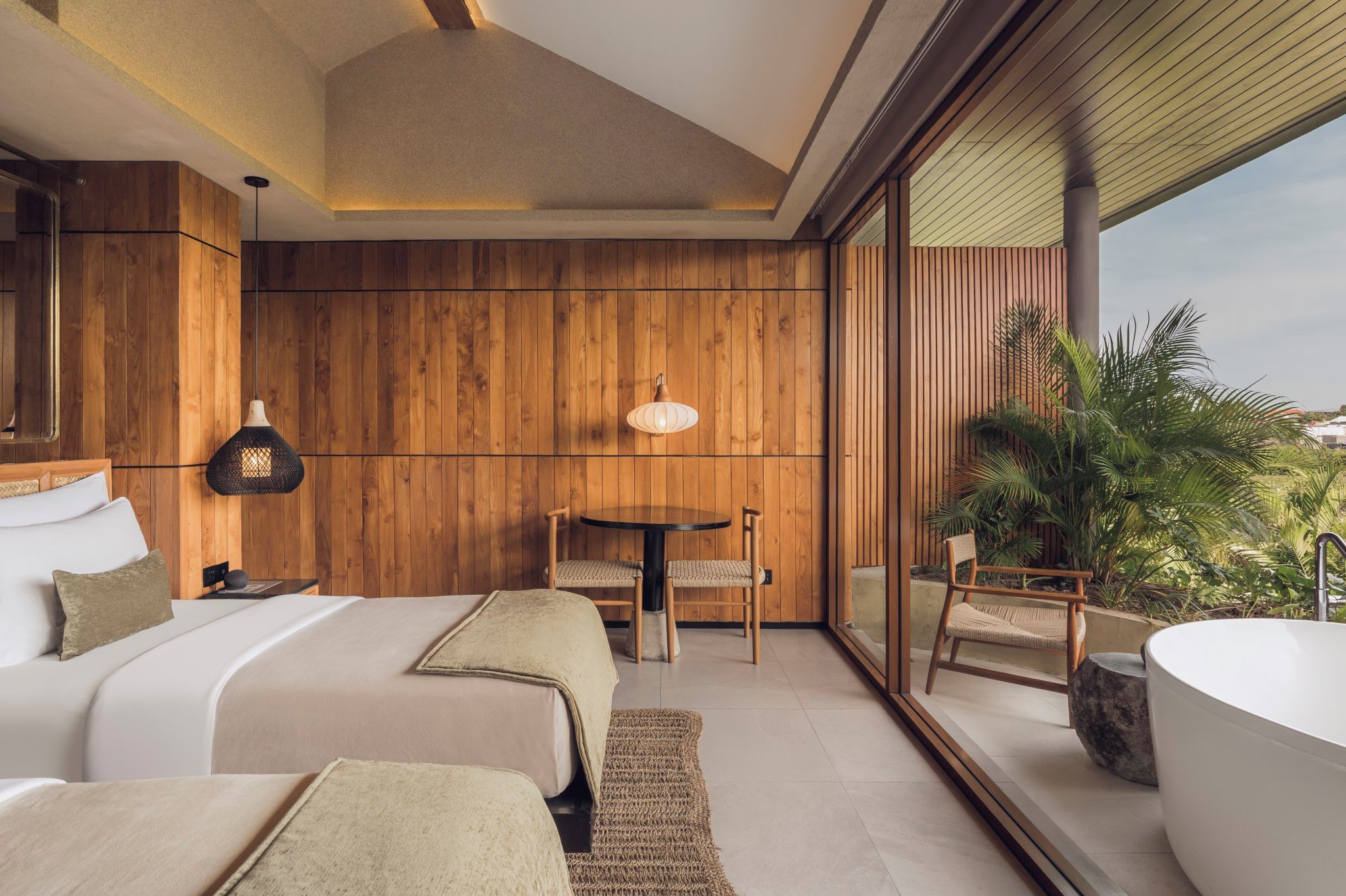 A modern bedroom with a large bed, two chairs, a round table, and a bathtub.
