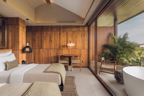 A modern bedroom with a large bed, two chairs, a round table, and a bathtub.