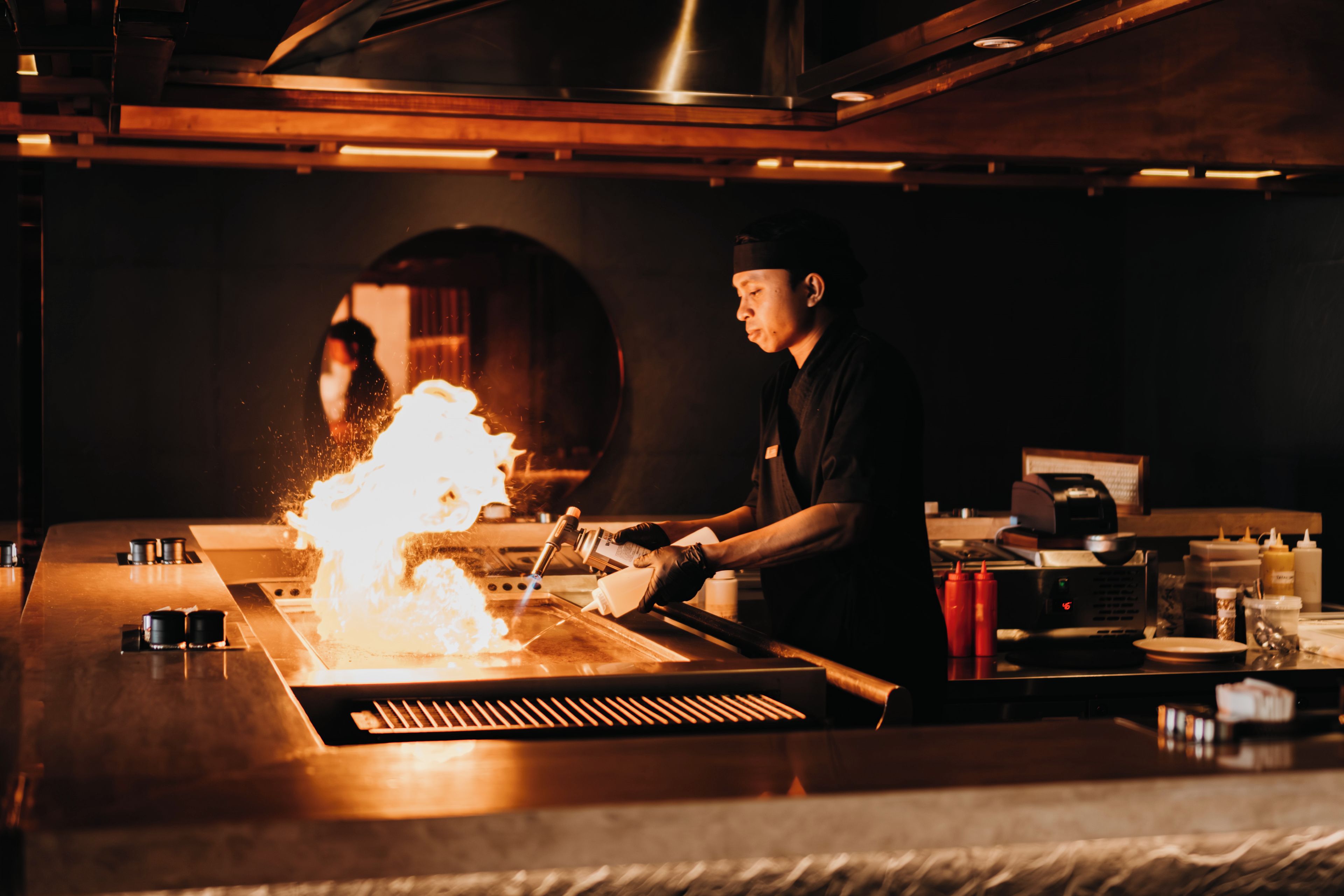 A chef cooking with a flame on a grill.