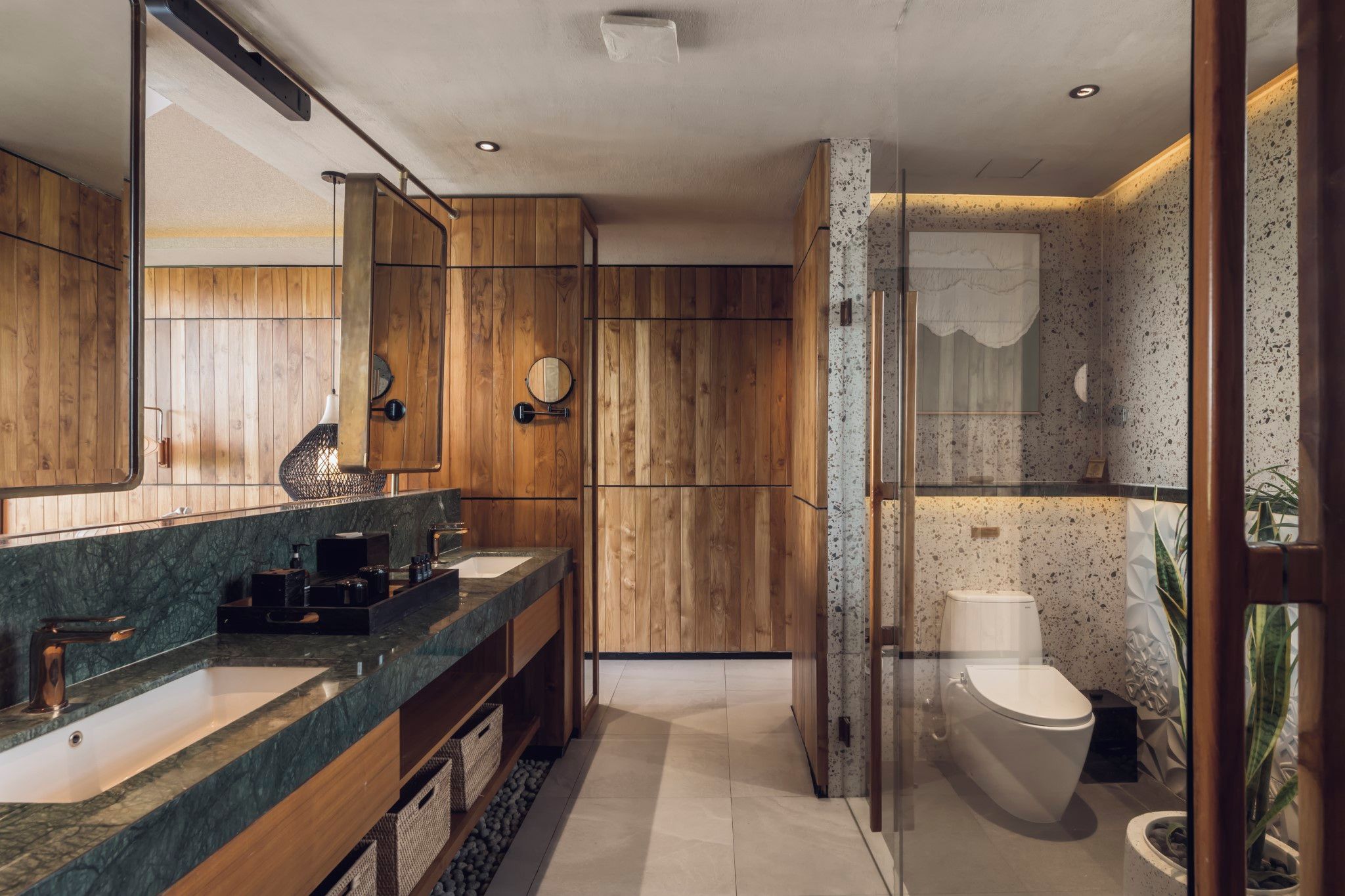 Ein modernes Badezimmer mit Holzvertäfelung, einem großen Spiegel, zwei Waschbecken und einer Toilette.