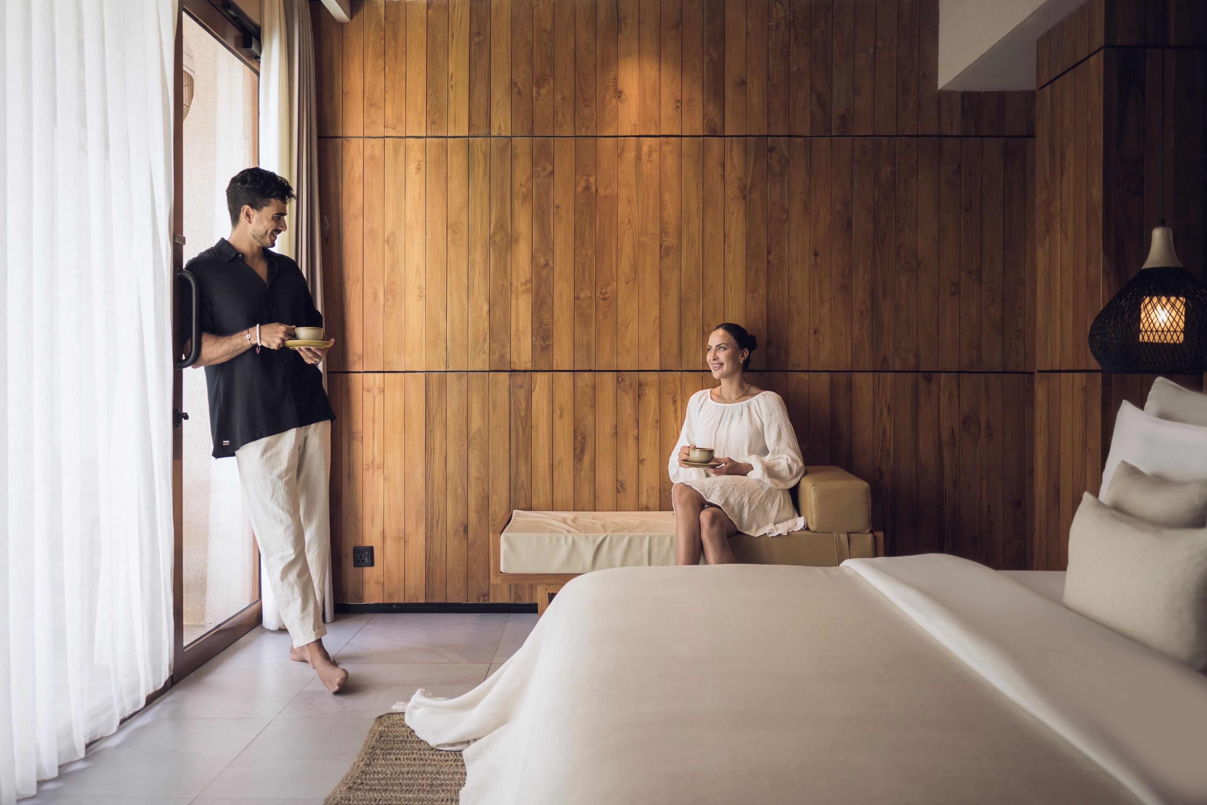 A room with a wooden wall, a bed, a sofa, and a person holding a bowl.