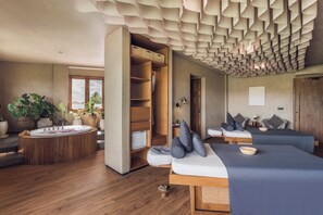 Una habitación de hotel moderna con suelo de madera, una bañera redonda, un sofá y una cama con almohadas.