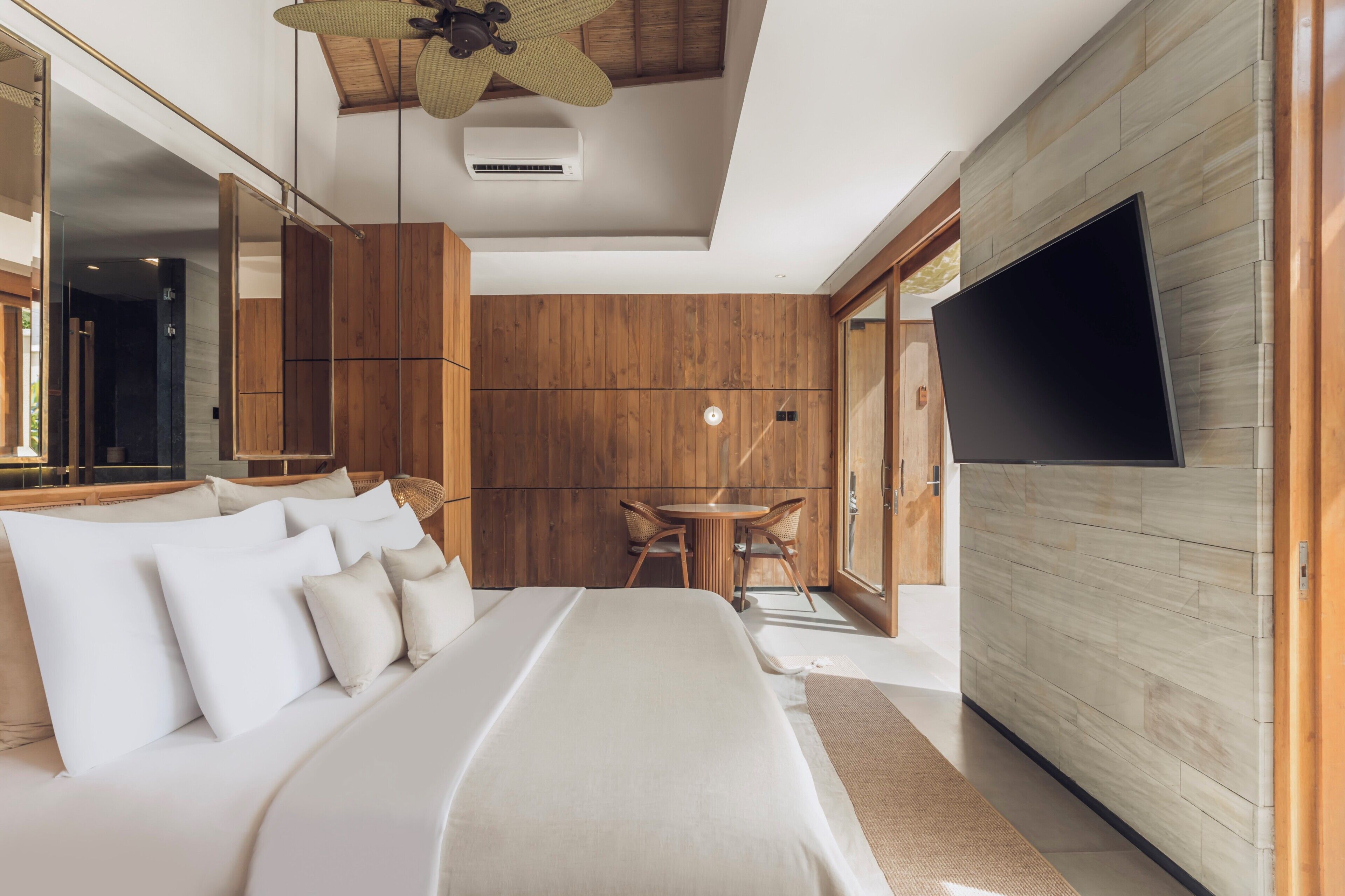Een moderne slaapkamer met een groot bed, een flatscreen televisie, een houten wand en een plafondventilator.