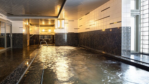 Un área de piscina interior moderna con suelo húmedo, paredes de azulejos y entrada por puerta de vidrio.