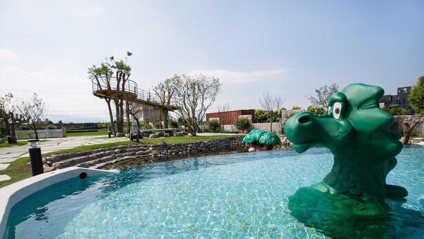 A swimming pool with a green dinosaur statue, a covered bridge, and a playground in the background. - Diu Diu Dang Family Homestay (Dongshan)