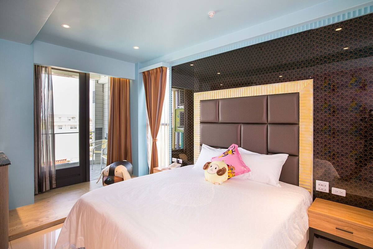 Habitación de hotel con una cama grande, cabecera, ventana con cortinas y vistas al exterior.