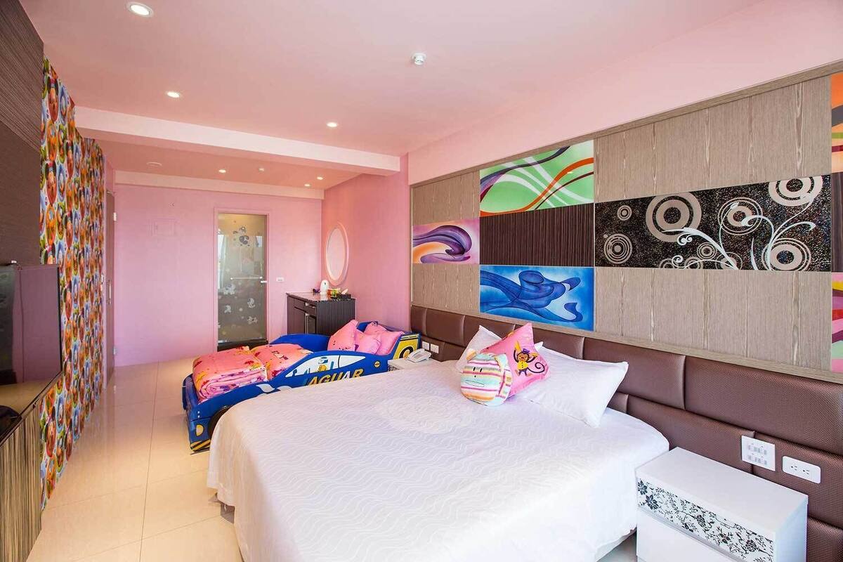 Habitación de hotel con dos camas, un espejo grande, una pared con arte abstracto y un cabecero de madera.