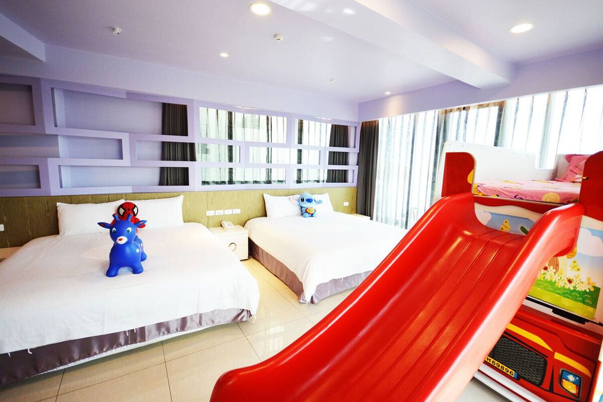 Una habitación de hotel con dos camas, un tobogán rojo y un coche de juguete.