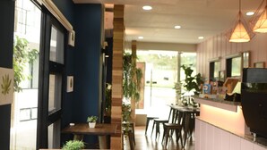 Un interior de restaurante moderno con mesas y sillas de madera, una zona de cocina con una parrilla y plantas en macetas.