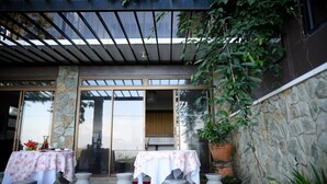 Un patio al aire libre con dos mesas cubiertas con manteles blancos, pilares de piedra y plantas en macetas.