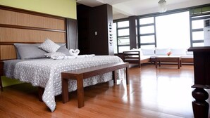 Un dormitorio con cama, mesita de noche, banco y sofá con vistas al exterior.