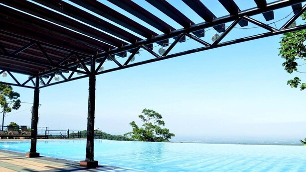 Una piscina infinita con vista despejada al horizonte, una estructura de pérgola y algunas sillas de descanso.
